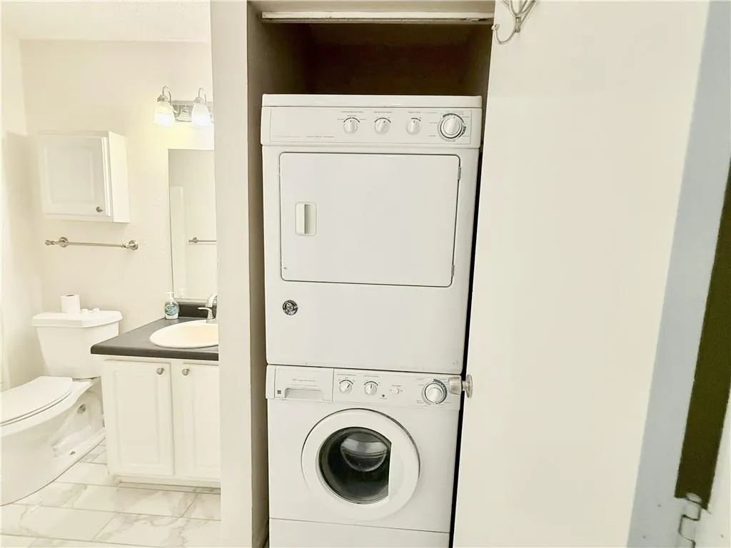 Laundry area with stacked washer / drying machine and light marble finish flooring