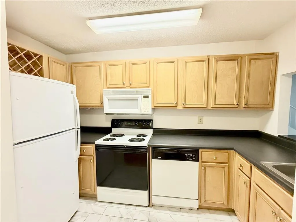 Kitchen featuring light brown cabinets, white appliances, light marble finish floors, and a textured ceiling
