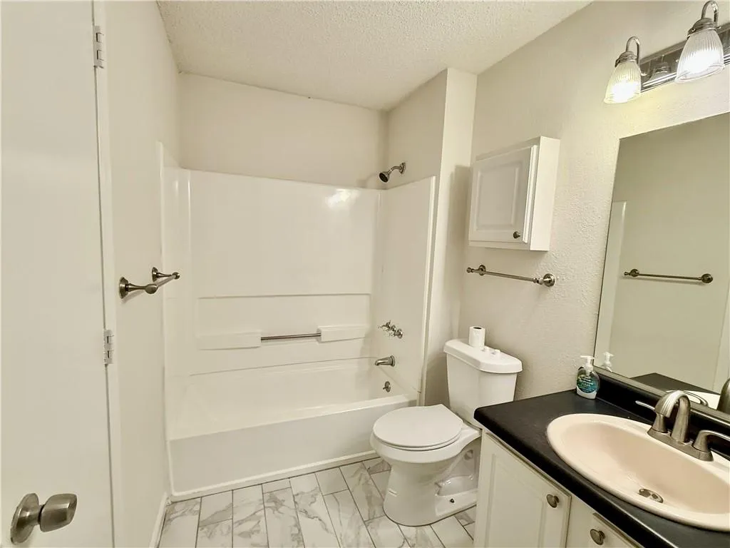 Full bathroom featuring marble look tile flooring, a textured ceiling, vanity, and shower / bath combination