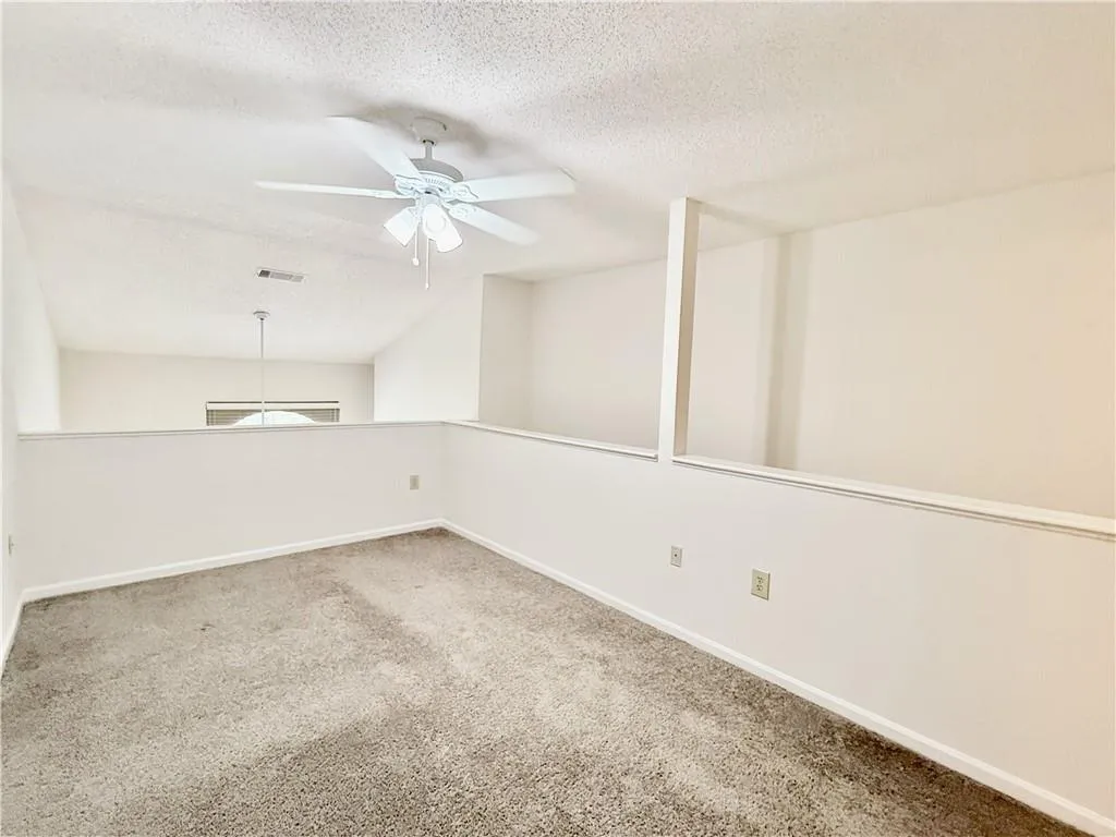 Empty room featuring a ceiling fan, a textured ceiling, and carpet flooring