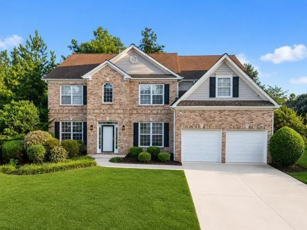 Brick facade home with a two-car garage, manicured lawn, and mature landscaping