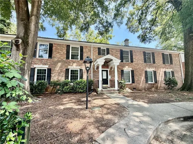 Brick facade with a covered entry, black shutters, and exterior lighting