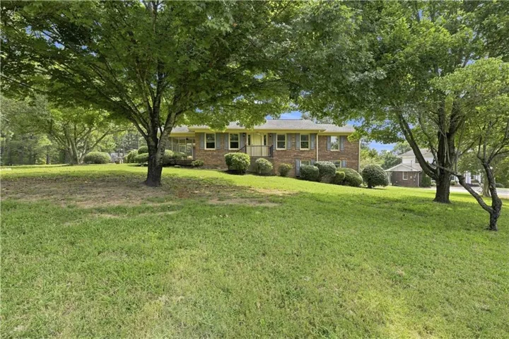 Brick exterior residence with a sloped front lawn and mature trees