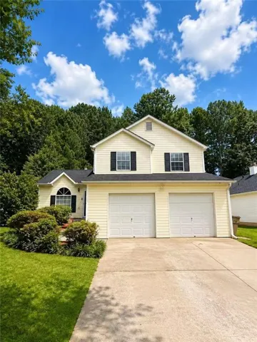 Two-story Colonial-style residence featuring cream-colored vinyl siding, dual two-car garage doors, and a concrete driveway