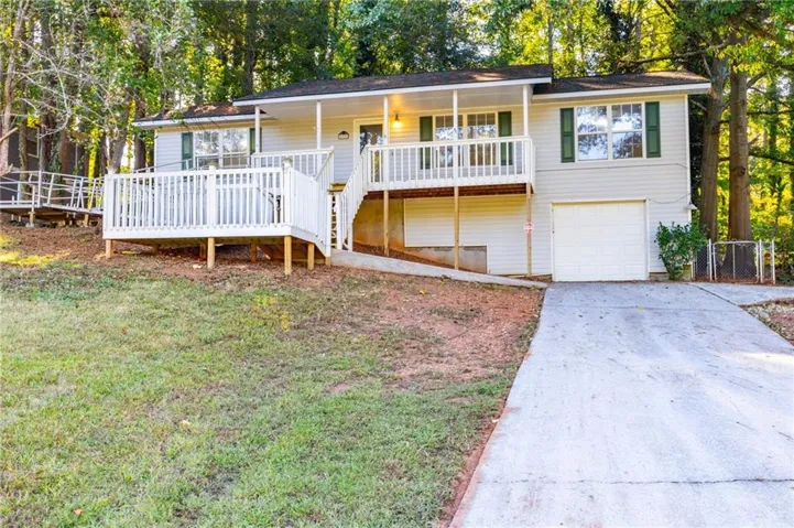 Ranch-style home with driveway, an attached garage, view of scattered trees, stairway, and a front lawn