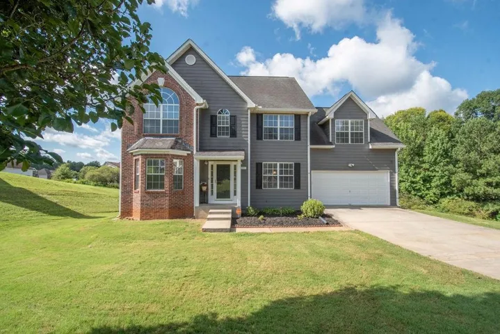 Two-story residence featuring a brick and siding exterior, an attached two-car garage, multiple gables, and a front entry with a covered porch
