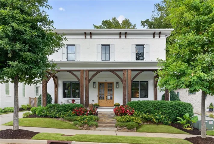 White brick exterior with black-framed windows, a covered porch with exposed wood beams, and a wood-paneled double-door entry