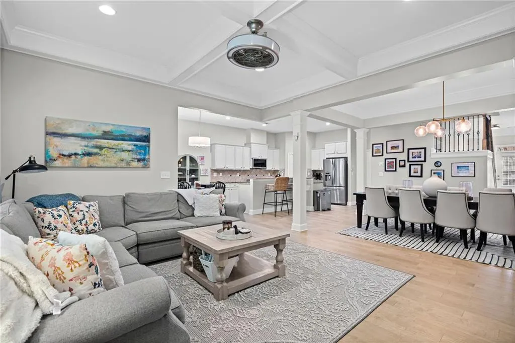 Living area with light wood-type flooring, ornamental molding, coffered ceiling, decorative columns, and suspended fan/light