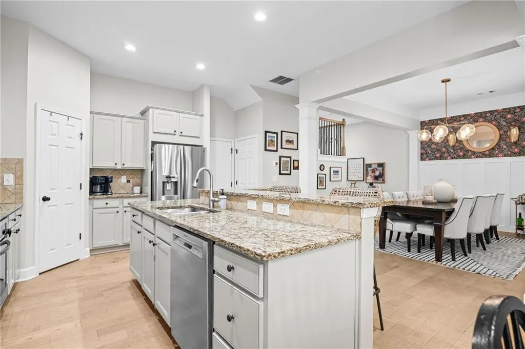 Kitchen featuring light stone countertops, a center island with sink, stainless steel appliances, light wood finished floors, and gray cabinetry