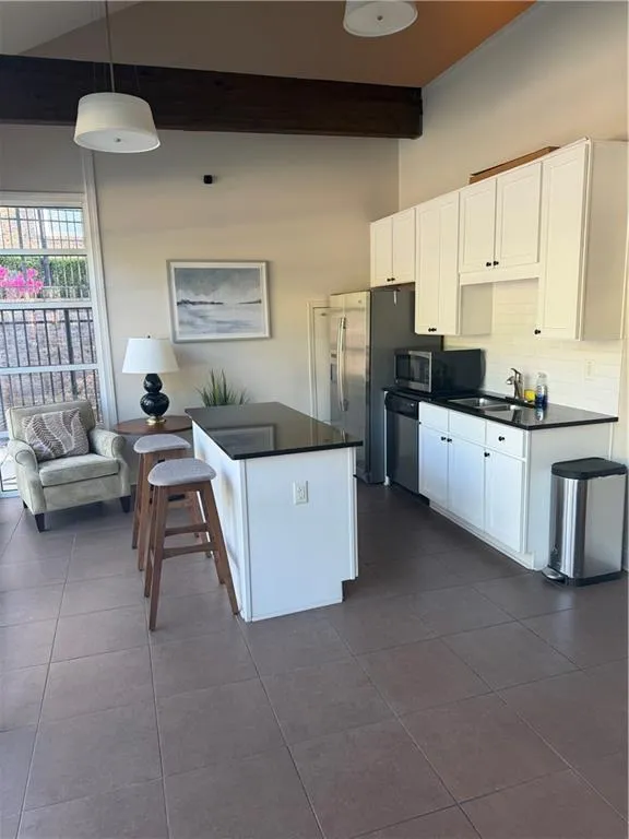 Clubhouse kitchen with white cabinetry, dark tile patterned floors, decorative backsplash, black microwave, and dishwashing machine