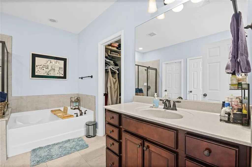Primary bathroom with a garden tub, a shower stall, a spacious closet, vanity, and light tile patterned floors