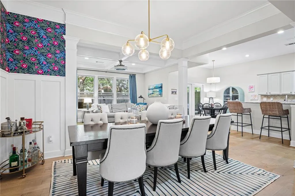 Dining area featuring light wood-type flooring, hanging lights, crown molding, beamed ceiling, and decorative columns