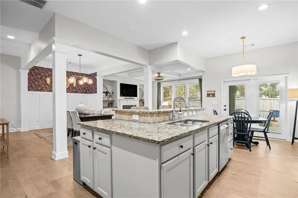 Kitchen featuring a wainscoted wall, light stone counters, a center island with sink, and light wood finished floors.
