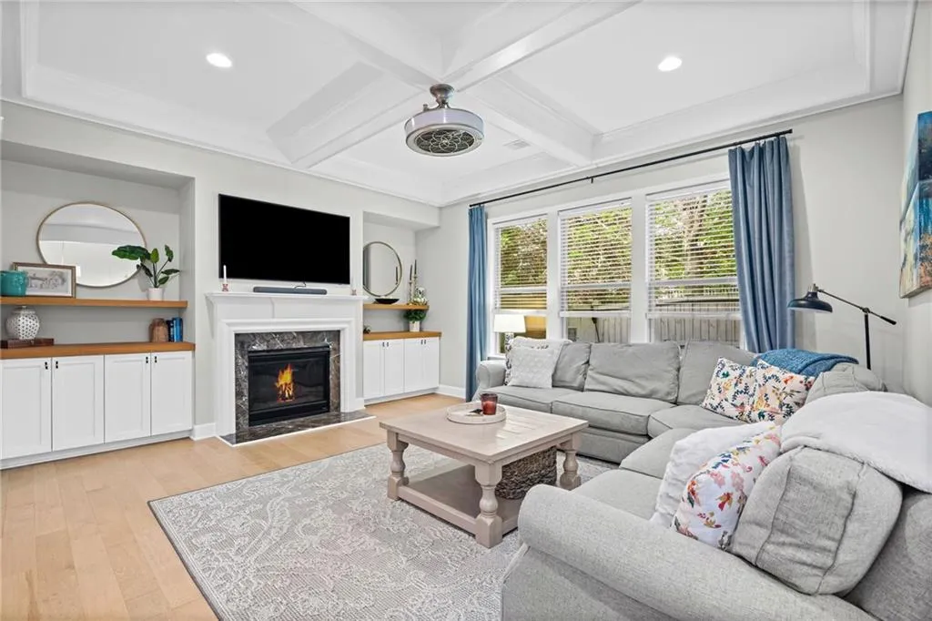 Living room with custom built-ins, coffered ceiling, a high end fireplace, light wood-style flooring, and recessed lighting