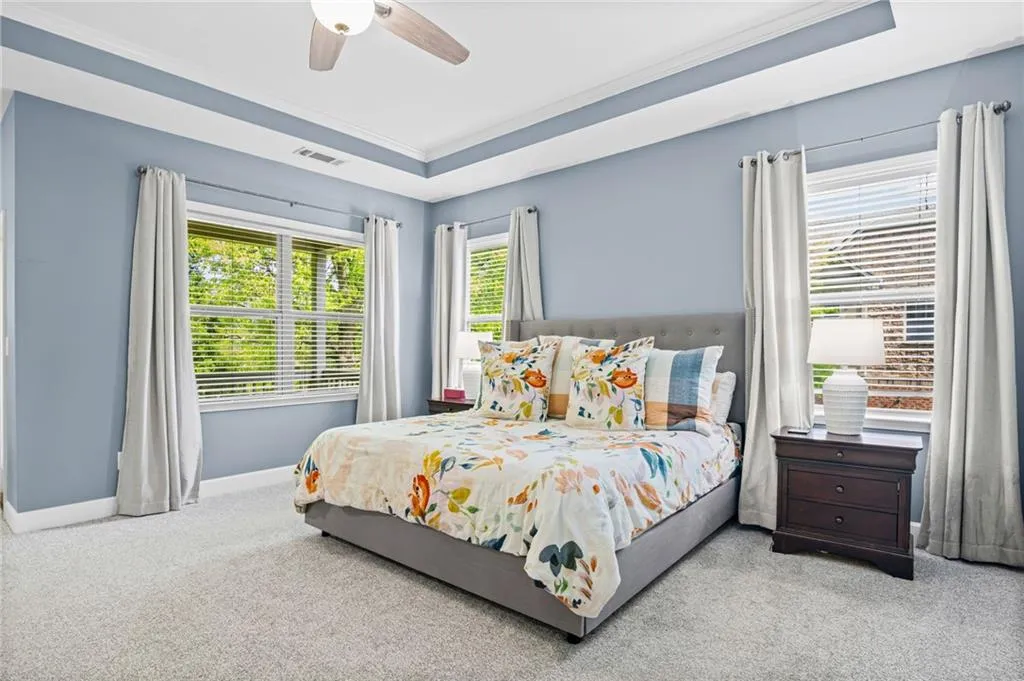 Primary bedroom featuring a tray ceiling, multiple windows, ornamental molding, and a ceiling fan
