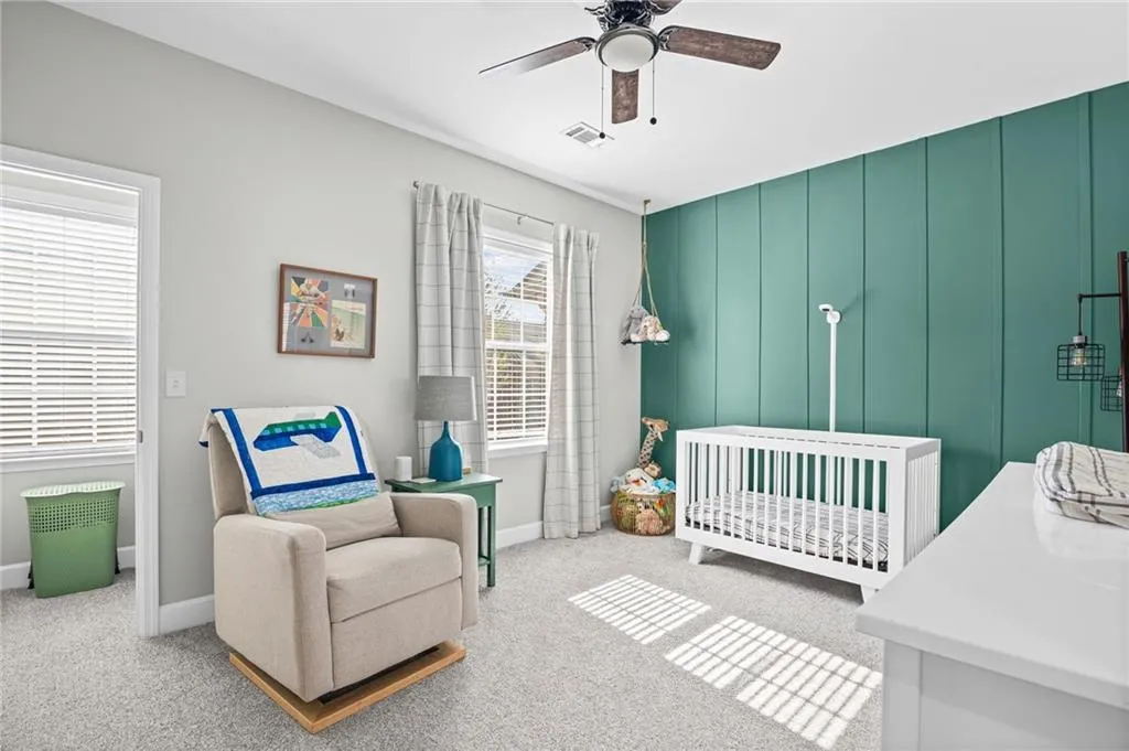 Bedroom featuring a nursery area, light carpet, and a ceiling fan