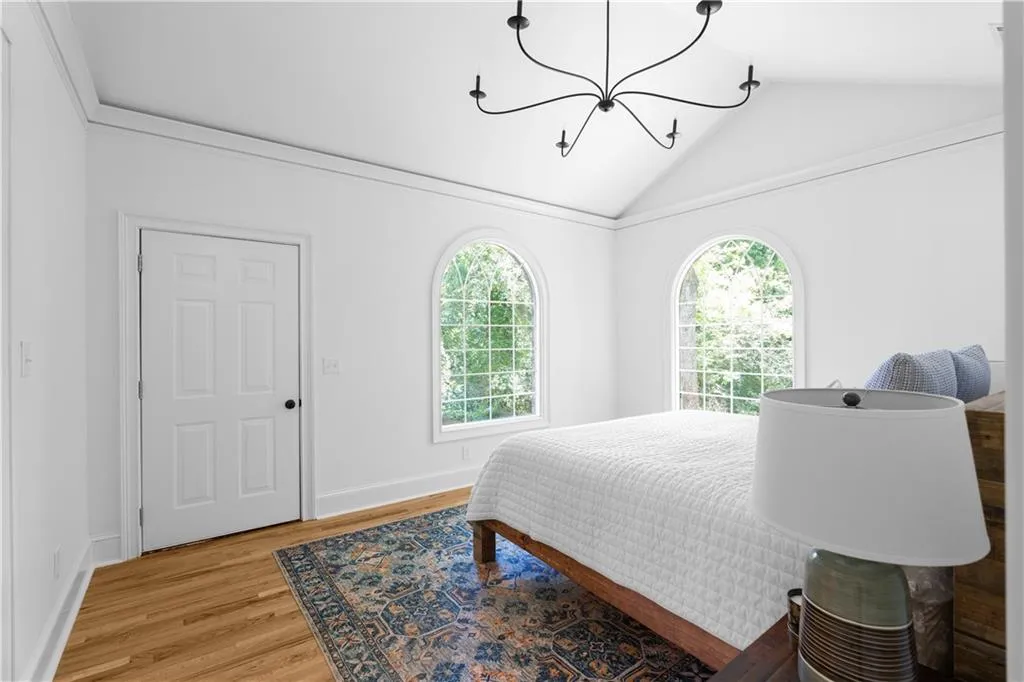 Bedroom featuring a chandelier, light wood-style floors, lofted ceiling, multiple windows, and baseboards