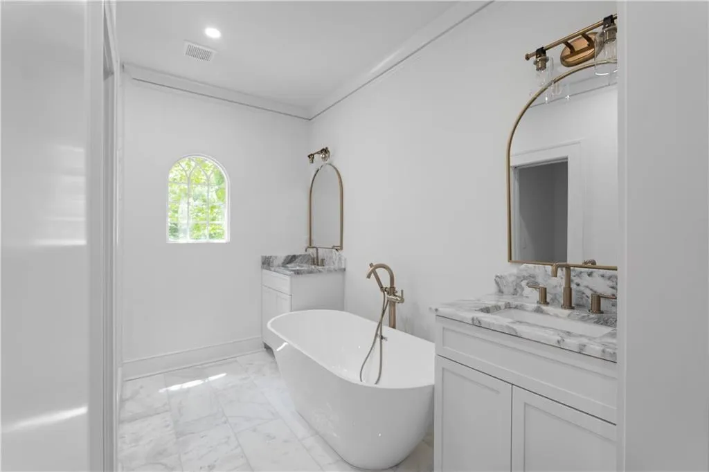 Full bath featuring marble finish flooring, a soaking tub, two vanities, baseboards, and recessed lighting