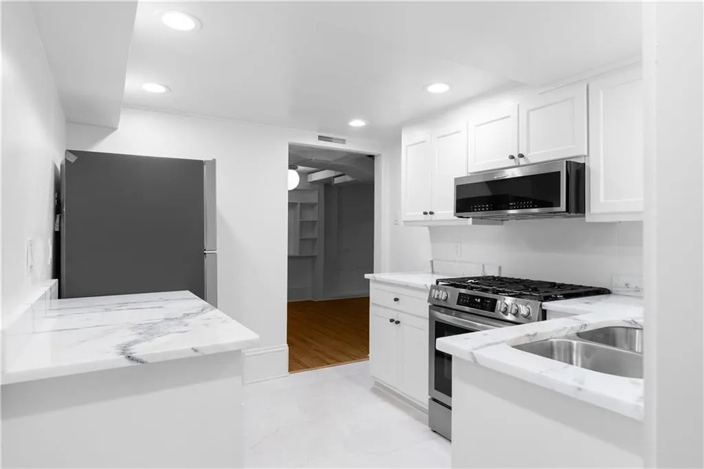 Kitchen with appliances with stainless steel finishes, white cabinets, light stone counters, recessed lighting, and a sink