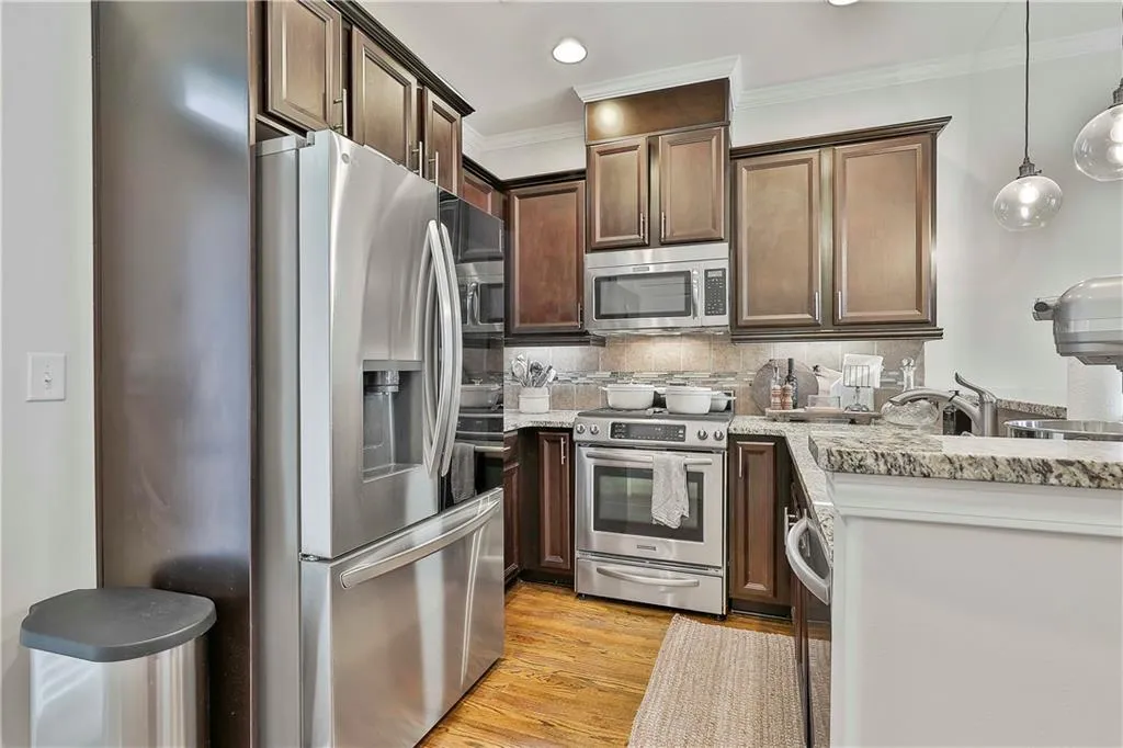 Kitchen with appliances with stainless steel finishes, light wood-type flooring, backsplash, pendant lighting, and crown molding