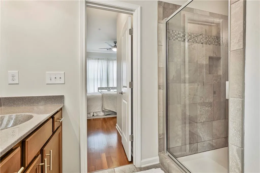 Ensuite bathroom featuring a shower stall, vanity, light wood-type flooring, and a ceiling fan