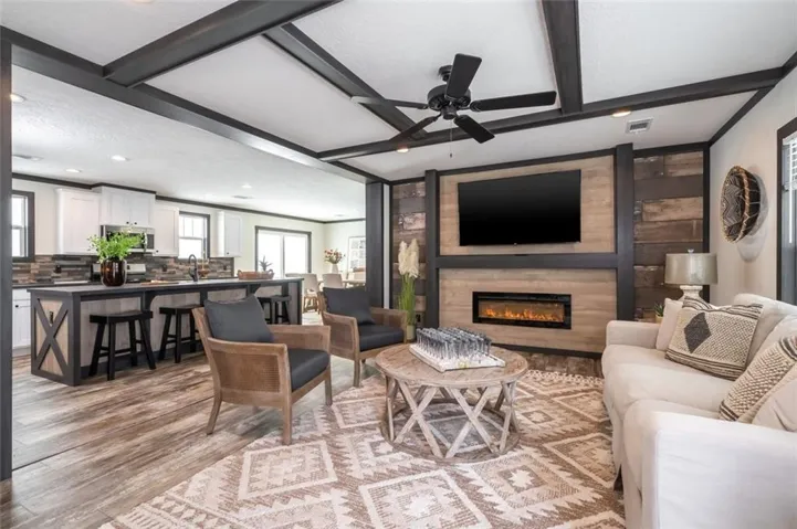Exposed beam ceiling, built-in media center with linear fireplace, wood-finish flooring, kitchen island with seating, and white cabinetry