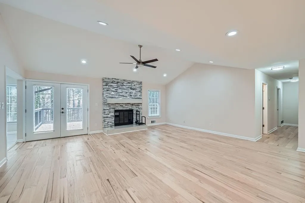 Unfurnished living room with a fireplace, baseboards, vaulted ceiling, french doors, and light wood-type flooring