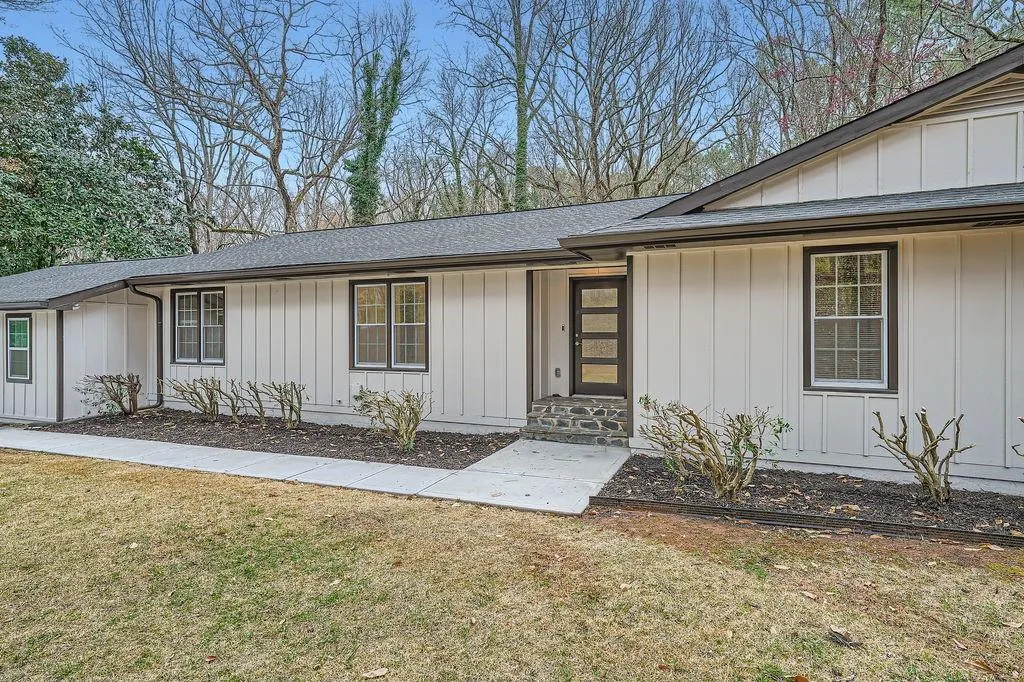View of exterior entry featuring a shingled roof, board and batten siding, and a lawn