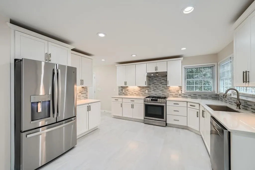 Kitchen featuring appliances with stainless steel finishes, light countertops, under cabinet range hood, white cabinetry, and a sink