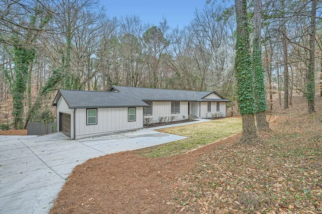 View of front of house with an attached garage, a shingled roof, driveway, a front lawn, and board and batten siding