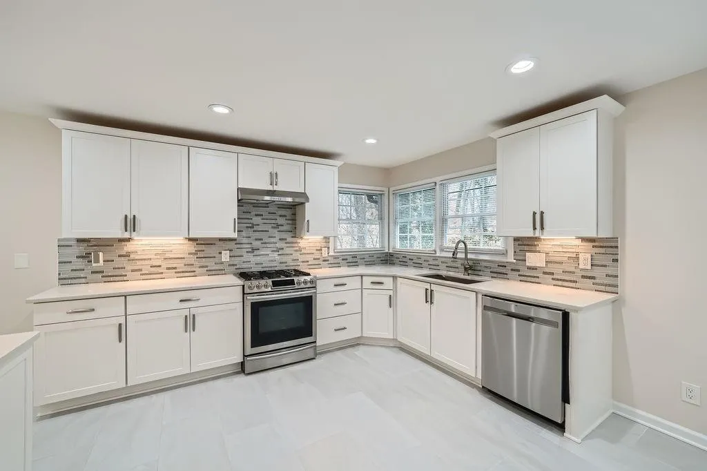 Kitchen featuring stainless steel appliances, light countertops, under cabinet range hood, white cabinetry, and a sink
