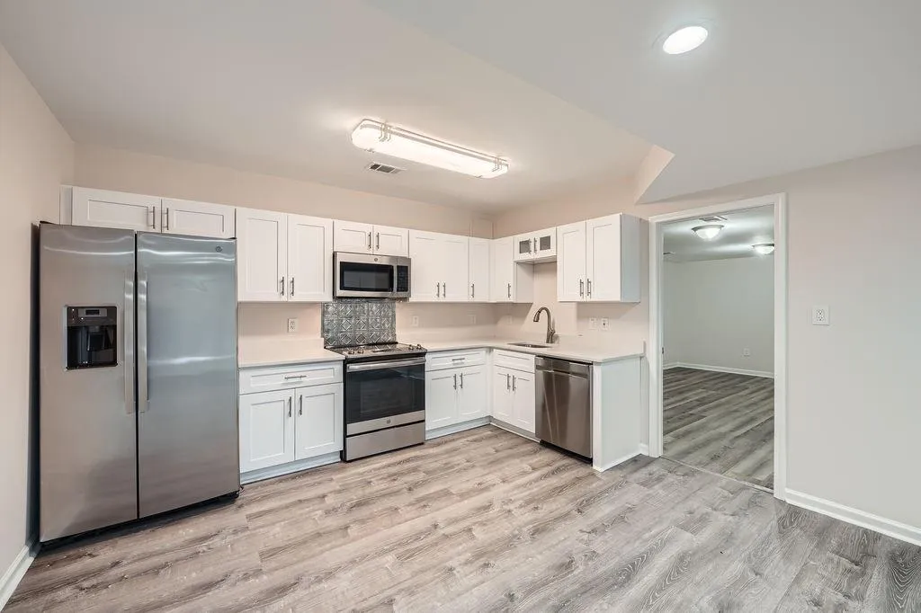 Kitchen with light wood finished floors, stainless steel appliances, light countertops, white cabinetry, and a sink