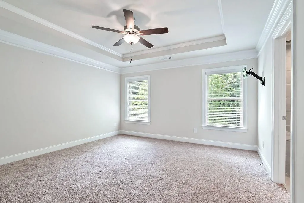 Spare room with ornamental molding, a raised ceiling, light colored carpet, and a ceiling fan