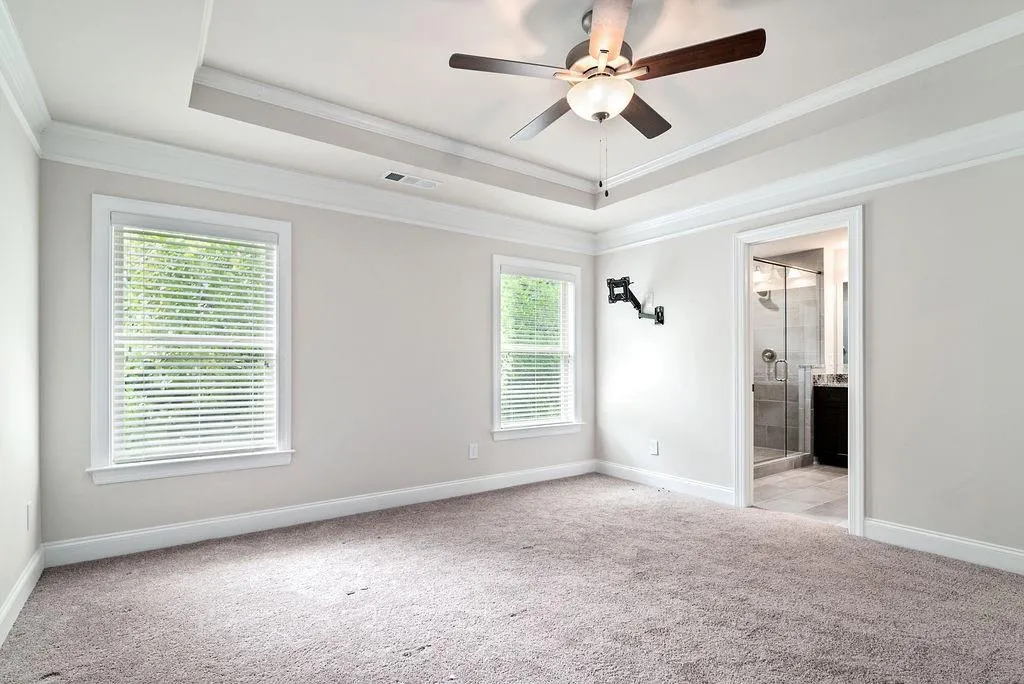 Empty room featuring light carpet, a raised ceiling, crown molding, and a ceiling fan