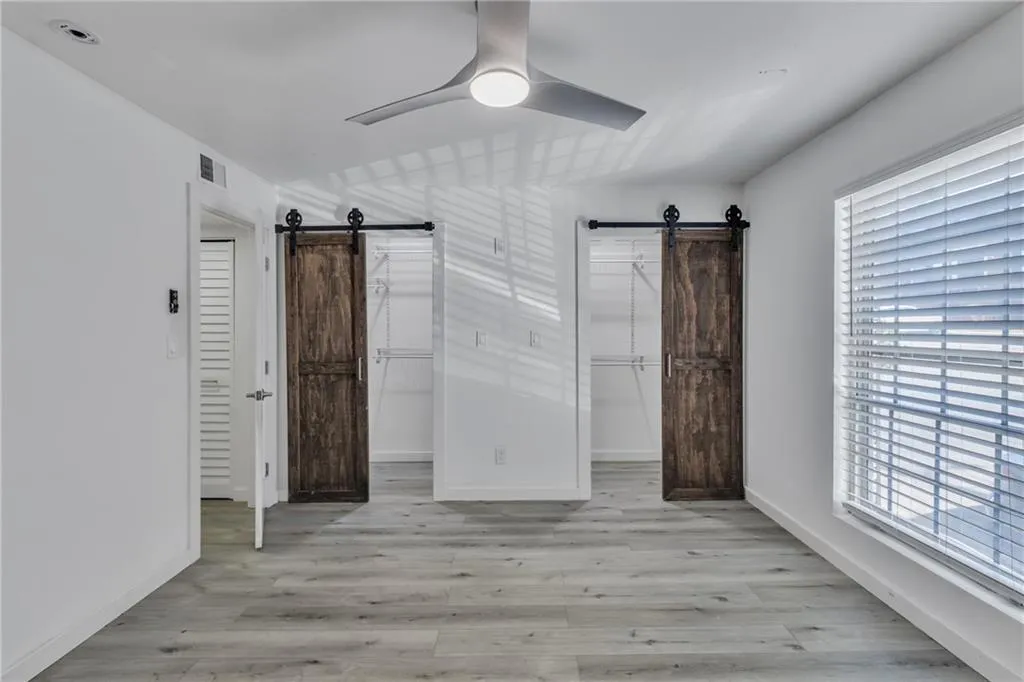 Unfurnished bedroom featuring a barn door, a walk in closet, light wood finished floors, and ceiling fan