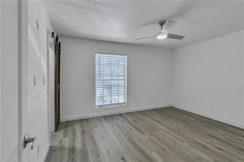 Unfurnished bedroom featuring a barn door, light wood-style floors, and ceiling fan