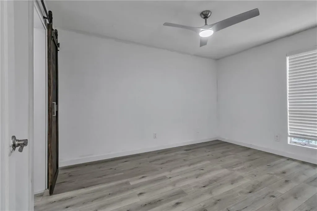 Empty room featuring a barn door, light wood finished floors, and a ceiling fan