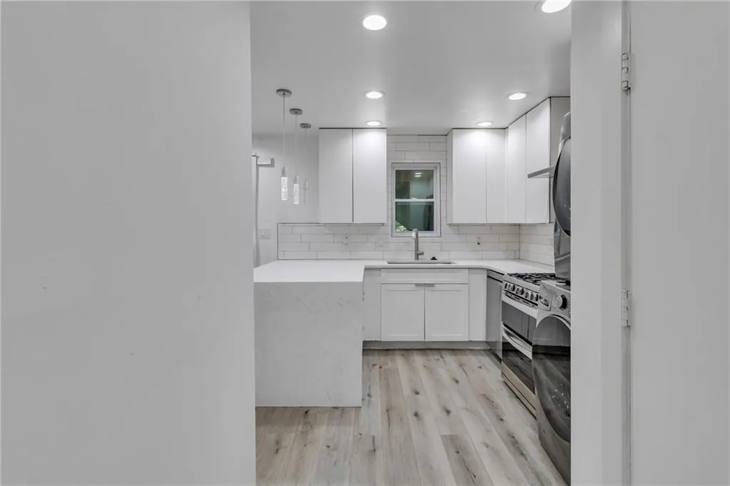 Kitchen with backsplash, light stone counters, white cabinets, light wood finished floors, and hanging light fixtures