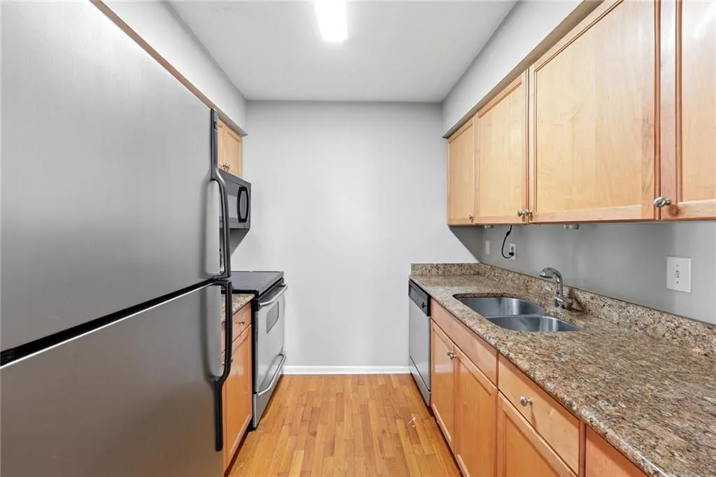 Kitchen featuring stainless steel appliances, dark stone counters, light wood-style floors, and light wood finish cabinetry