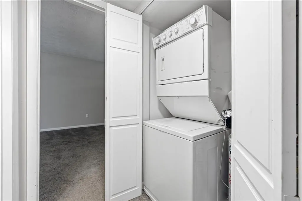Laundry area with stacked washer and clothes dryer and light colored carpet