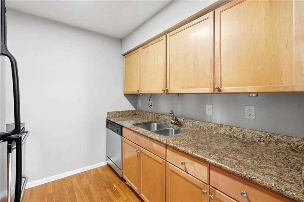 Kitchen with light stone countertops, light wood finish cabinets, dishwasher, light wood-type flooring, and stove