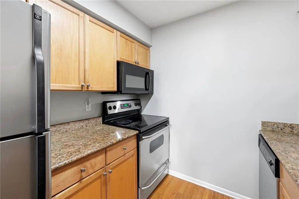 Kitchen with stainless steel appliances, light wood-style floors, light stone countertops, and light wood finish cabinets