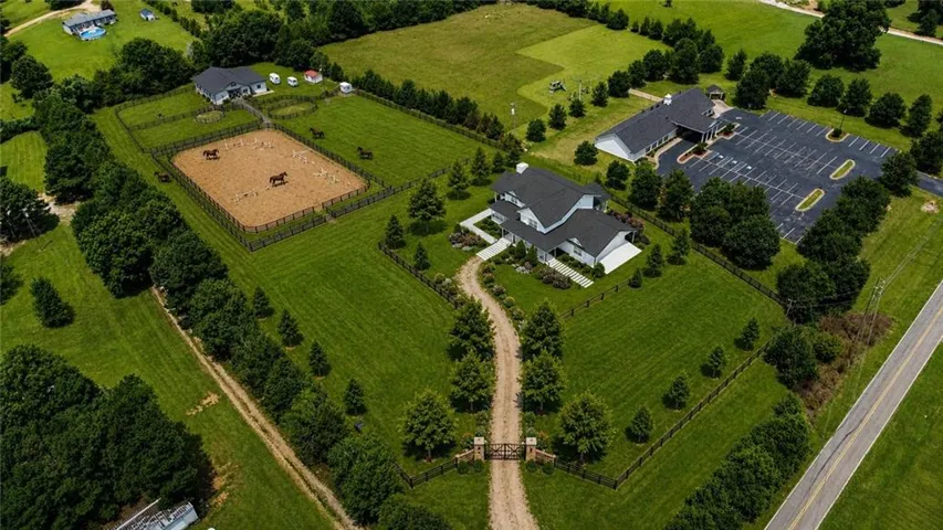 Expansive property featuring multiple structures, extensive green space, a fenced equestrian arena, gated entry, and a large paved parking area