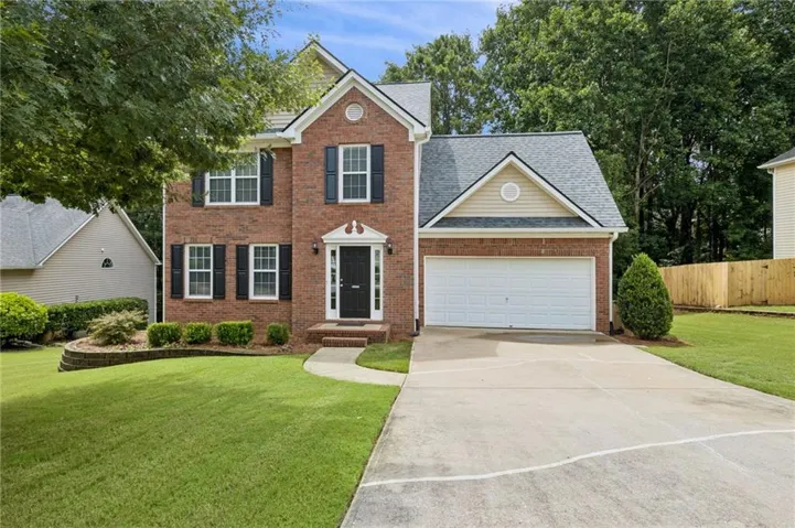 Traditional brick two-story home featuring a gabled roofline, front-facing two-car garage, manicured lawn, and a stone-edged planting bed