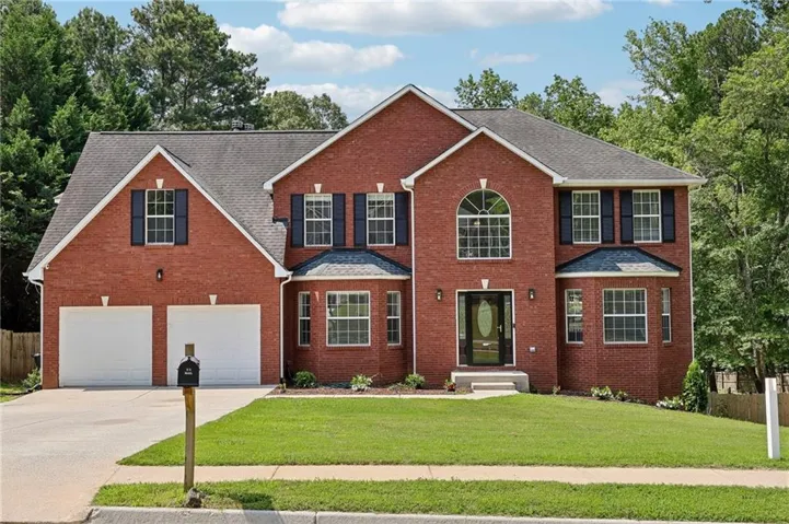 Brick facade residence featuring a two-car garage, arched entry window, dark shutters, covered front entry, and a manicured lawn