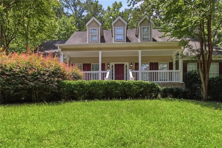 Traditional-style home featuring a covered front porch with white railings and columns, dormer windows, and a red front door