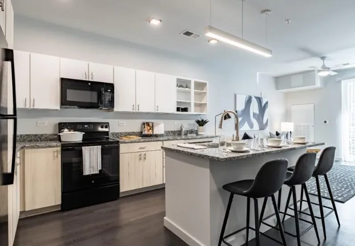 Kitchen featuring black appliances, a breakfast bar, dark stone counters, an island with sink, and ceiling fan