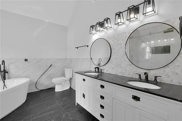 Dual vanity with black countertops and undermount sinks, freestanding soaking tub, black tile flooring, and white hexagonal wall tiling