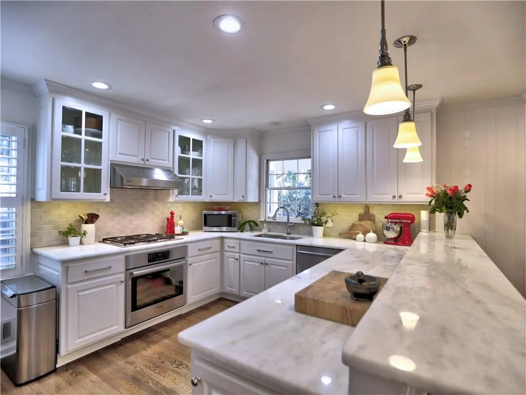 Kitchen with sink, white cabinetry, hanging light fixtures, stainless steel appliances, and kitchen peninsula