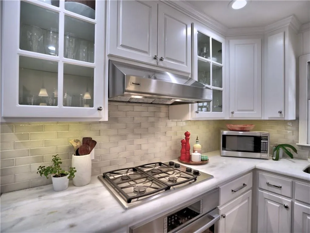 Kitchen with white cabinetry, stainless steel appliances, ventilation hood, and decorative backsplash